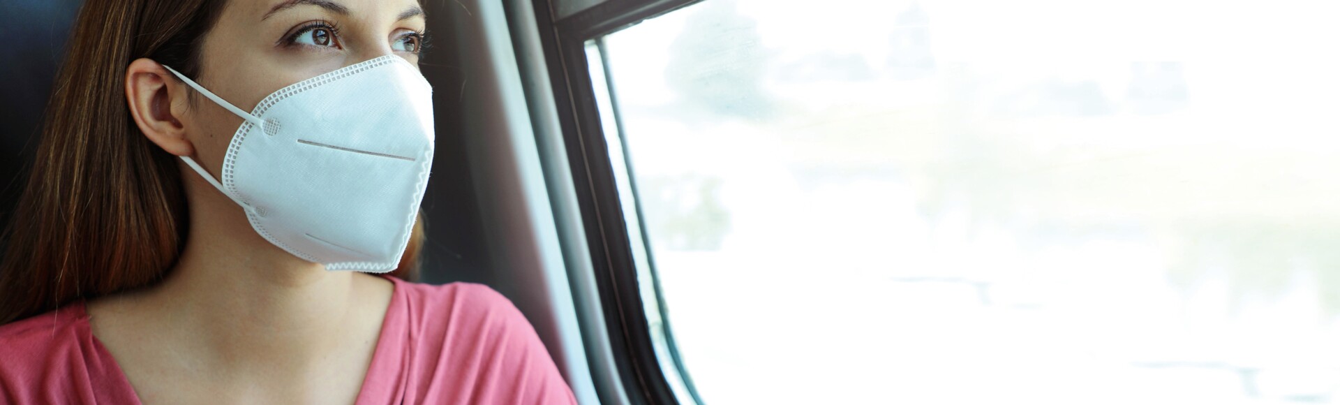 Frau mit Maske sitzt im Zug vorm Fenster
